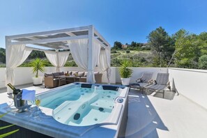 Eine Dachterrasse mit Whirlpool, Liegestühlen, einer überdachten Lounge und Topfpflanzen.