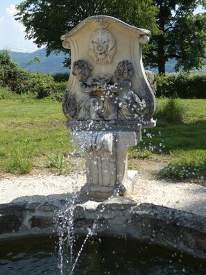 A stone fountain with water spouting from its center, surrounded by a grassy area and trees. - Guest Room “Chambre De La Fontaine” with Shared Terrace, Garden, and Wi-Fi (Saint-Albin-de-Vaulserre)
