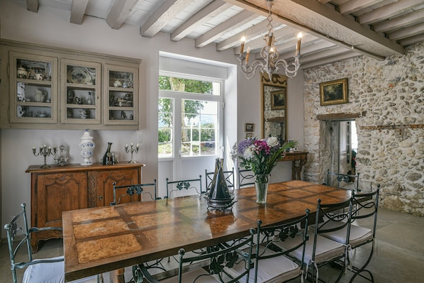 Un espace repas comprenant une table en bois, des chaises en métal, un lustre et un mur en pierre.