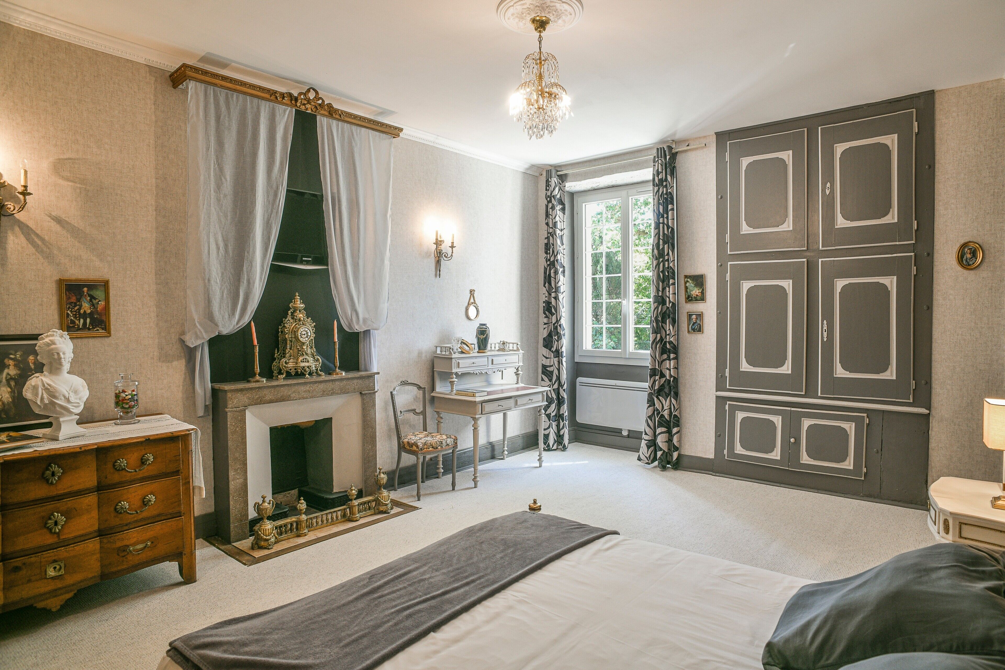 A bedroom with a bed, dresser, vanity, and a fireplace.