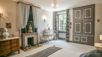 A bedroom with a bed, dresser, vanity, and a fireplace.