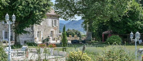 A stone building with a garden, outdoor seating, and a view of mountains.