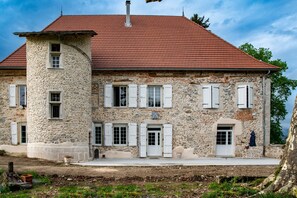 Een gebouw van steen met een rood dak, witte luiken en een klein terras.