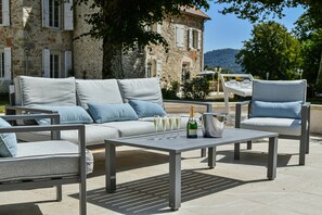 Un espacio al aire libre con sillones, sofás y una mesa con vasos y una botella.