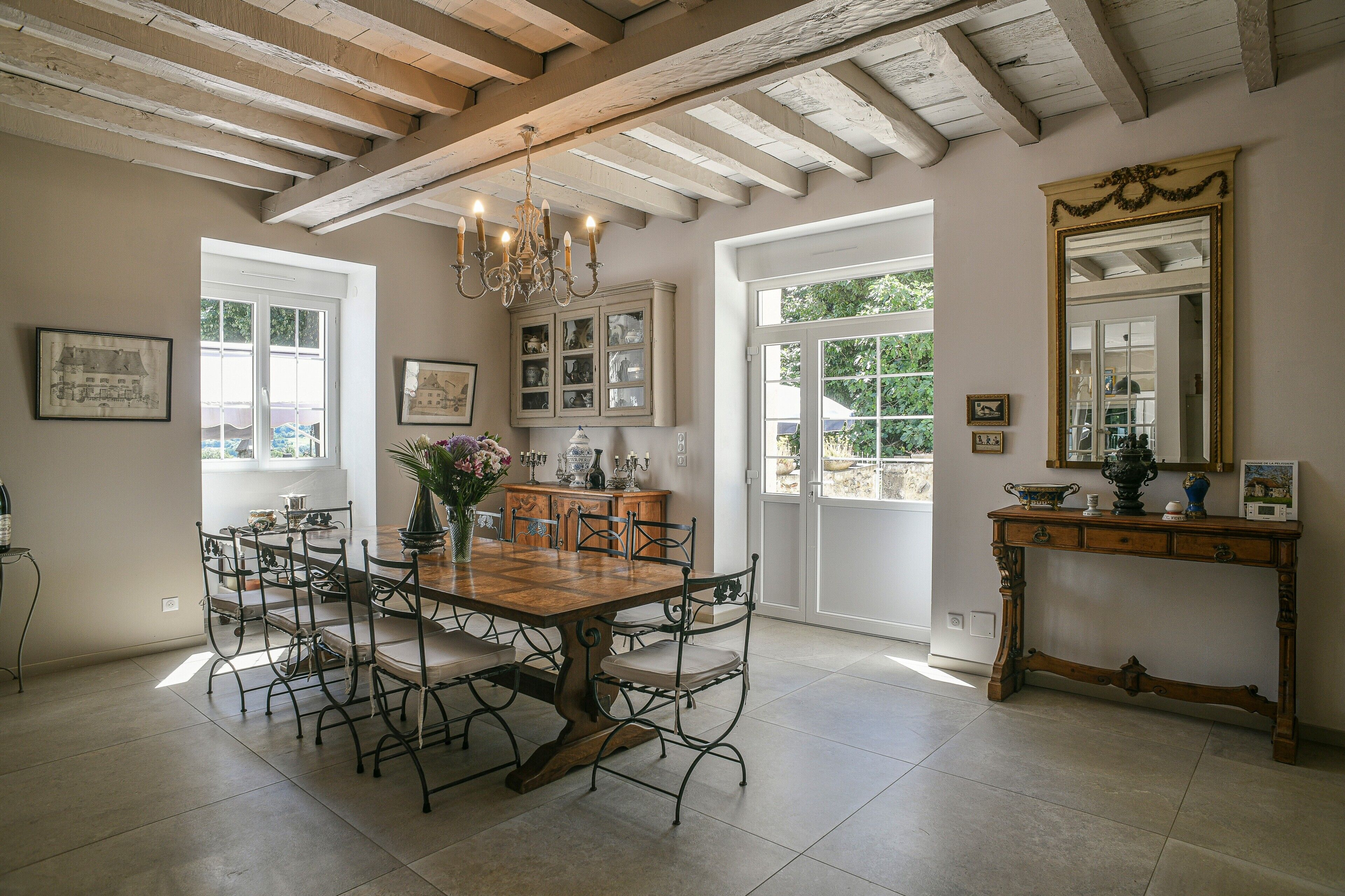 Une salle à manger avec une grande table en bois, des chaises en métal, un lustre et un miroir posé sur une console.