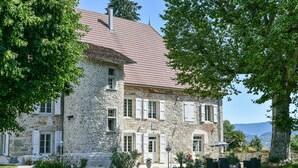 A stone building with a tiled roof, multiple windows, and a garden area with outdoor seating.