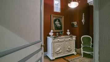 A hallway with a white ornate cabinet, a green upholstered chair, and a framed portrait on the wall.