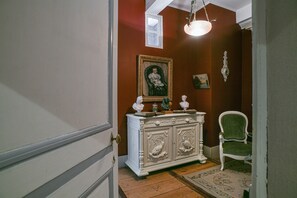 A hallway with a white ornate cabinet, a green upholstered chair, and a framed portrait on the wall.