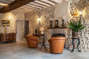 Una habitación de paredes de piedra con chimenea, sillones de cuero, un aparador de madera y una planta en maceta.