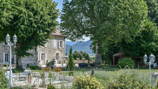 Un edificio de piedra con jardín, mesas al aire libre y vistas a montañas.
