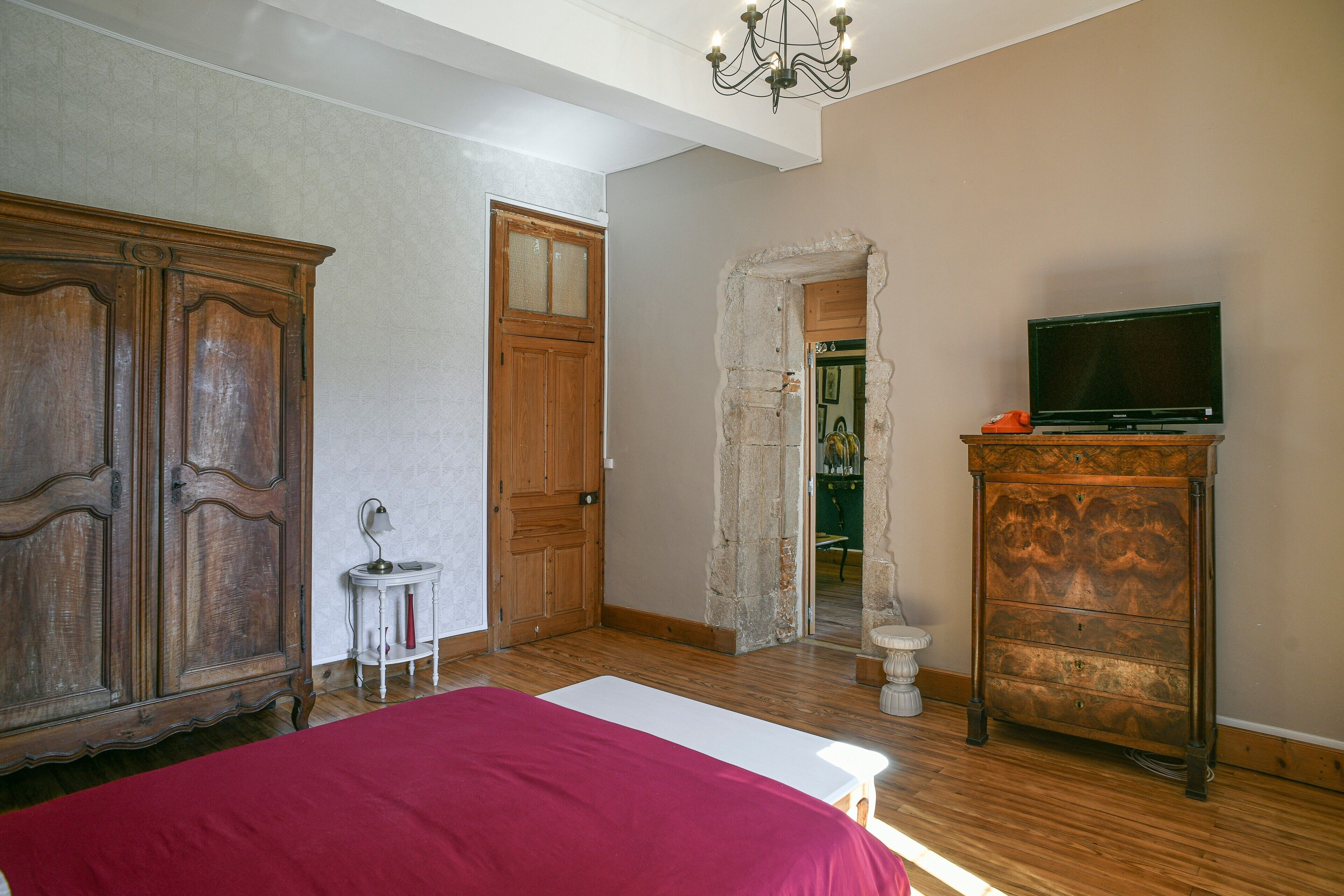 A bedroom with a bed, wooden wardrobe, television, and a small table.