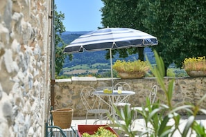 A stone wall, a white metal table with chairs, a striped umbrella, and a view of the countryside. - Guest Room “Chambre du Parc”: Mountain View, Shared Terrace, Wi-Fi (Saint-Albin-de-Vaulserre)