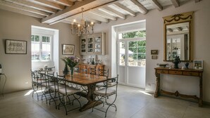Un comedor con una gran mesa de madera, sillas de metal, una araña y un espejo sobre un aparador.