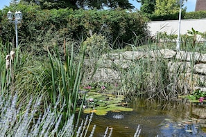 A pond with water lilies and tall grasses, surrounded by lush greenery and a white wall. - Guest Room “Chambre du Parc”: Mountain View, Shared Terrace, Wi-Fi (Saint-Albin-de-Vaulserre)