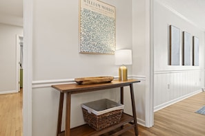 A hallway with a wooden console table, a lamp, a framed artwork, and a wicker basket. - Pebble Creek Cottage (Taylors)