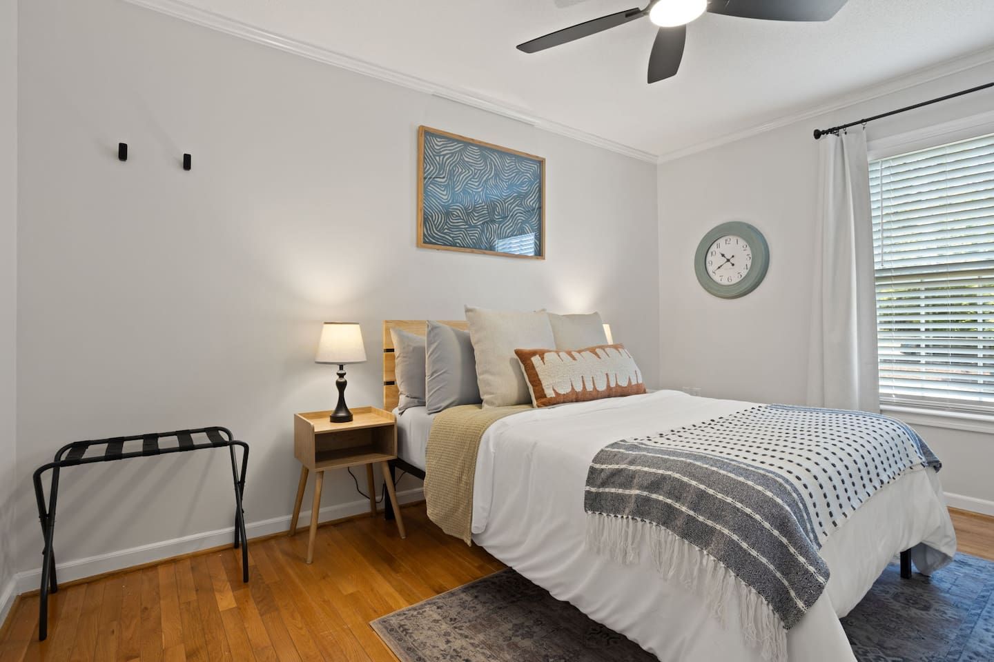A bedroom with a bed, bedside tables, a lamp, a clock, and a ceiling fan.