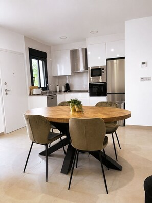 A modern kitchen with white cabinets, stainless steel appliances, and a round dining table with chairs. - 2-bedroom-2 bathroom apartment in San Pedro Del Pinatar with shared pool and AC (San Pedro Del Pinatar)