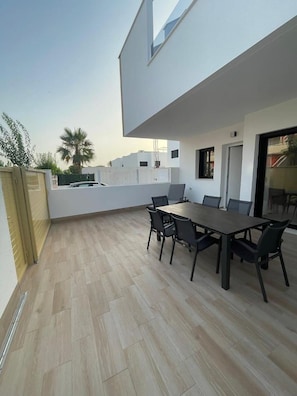 Eine moderne Außenpatio mit Esstisch und Stühlen, einem Holzboden und einem weißen Gebäude im Hintergrund.