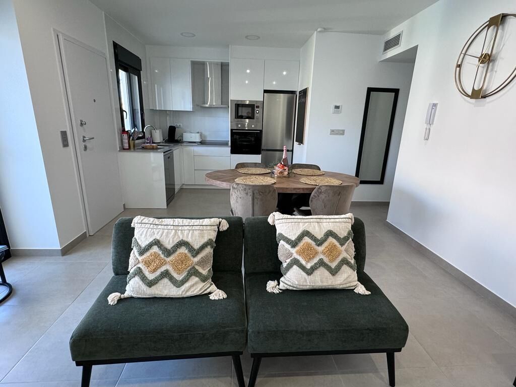 A modern kitchen with white cabinets, a stainless steel refrigerator, and a dining table with four chairs.