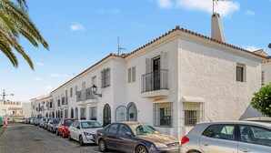 A row of parked cars along a street with white buildings featuring balconies and shutters. - Casa Mirador Information (Conil de la Frontera)