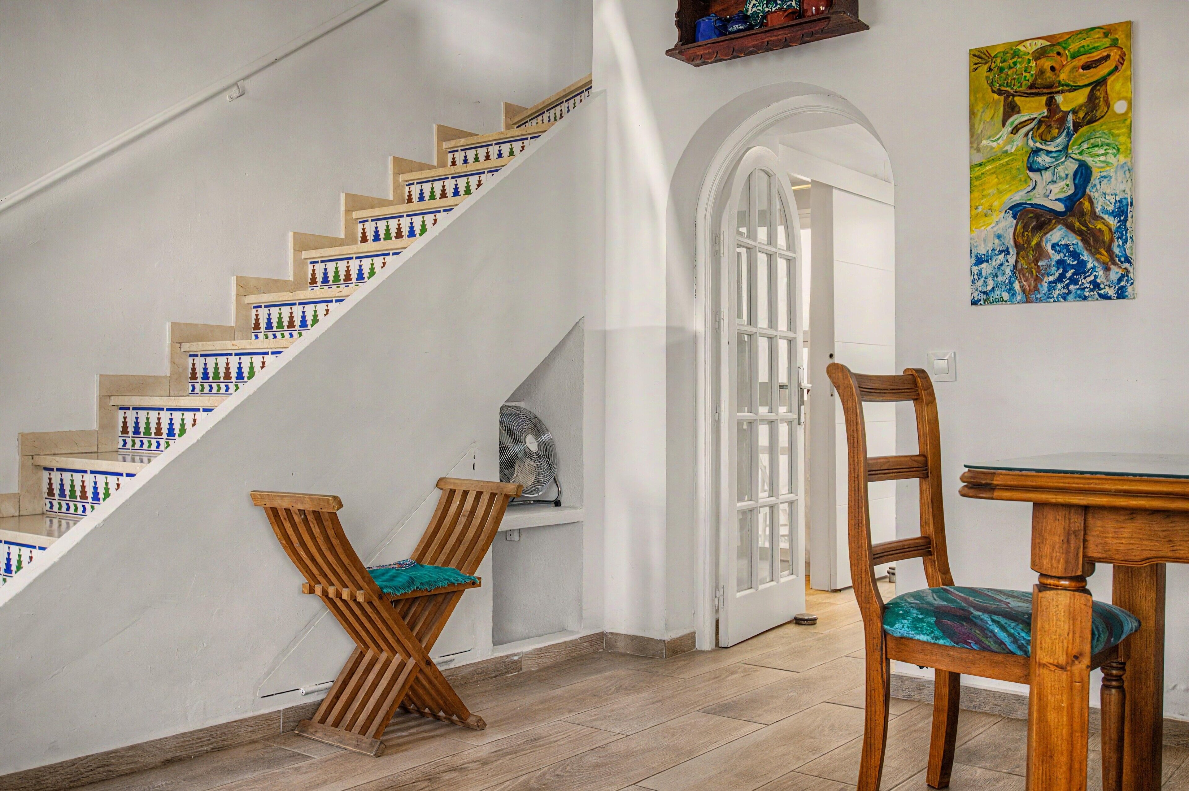 A staircase with patterned steps, a wooden chair with a cushion, a dining table, and a painting on the wall.