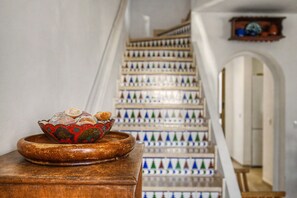 Un escalier orné d’une rampe décorative et un récipient contenant des coquillages, posé sur une table en bois.
