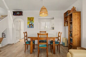 Un coin repas avec une table et des chaises en bois, un luminaire suspendu, un tableau au mur et une bibliothèque contenant divers objets.