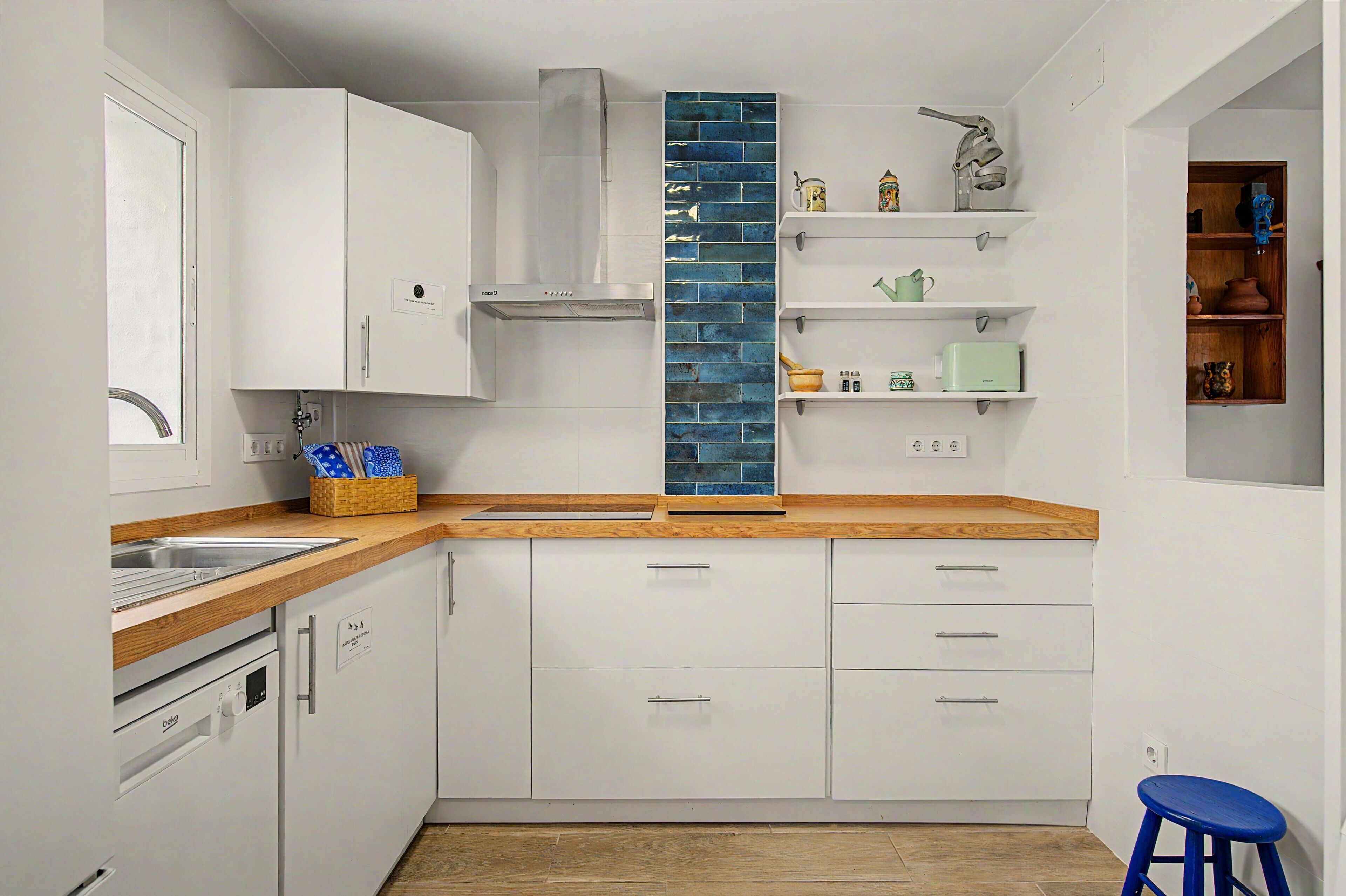 A modern kitchen with white cabinets, a wooden countertop, a blue backsplash, and a built-in stove.