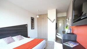 A modern hotel room with a bed, a desk, a television, and a mirror.