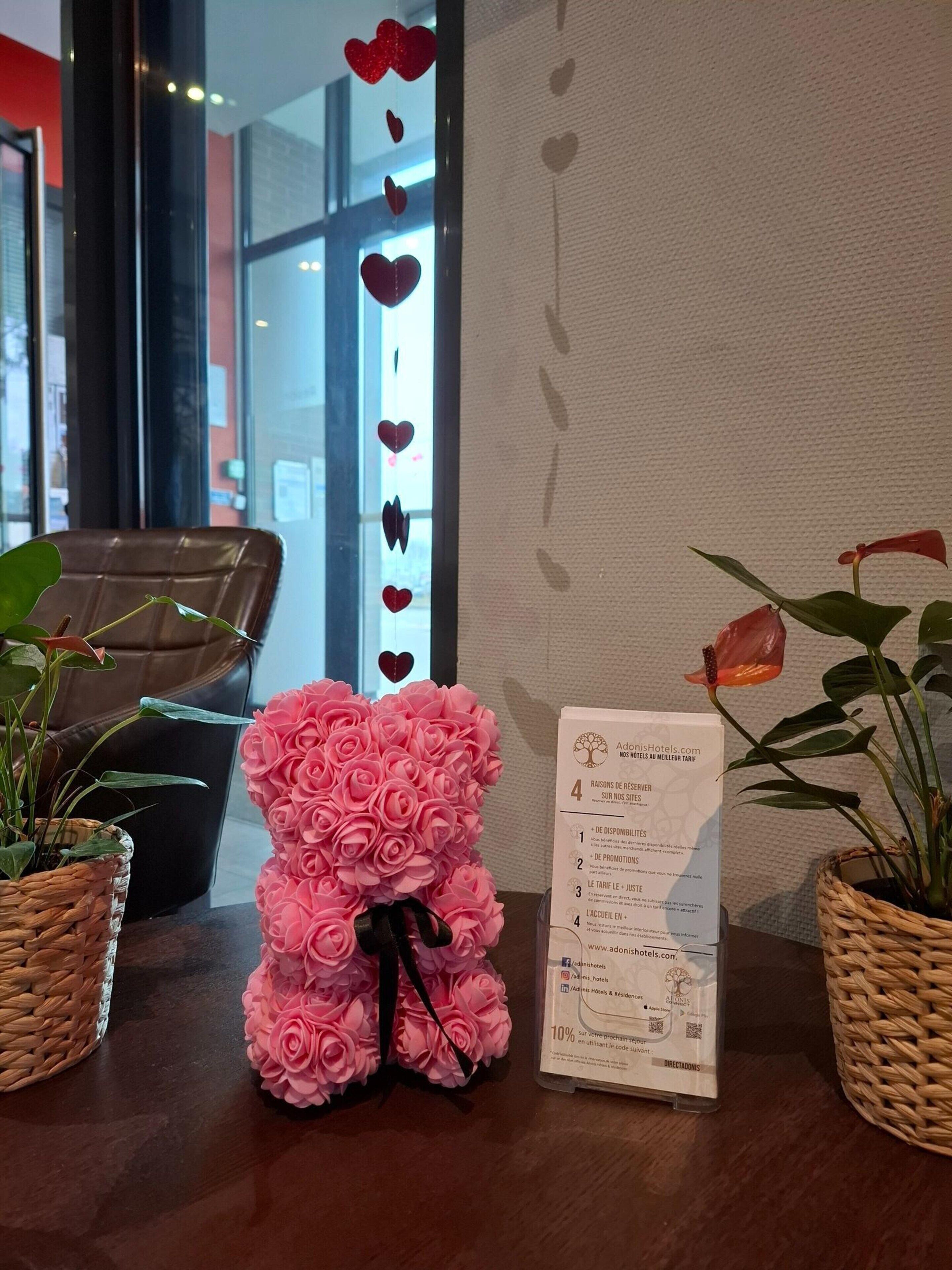 A reception desk with a pink flower arrangement, a printed document, and two potted plants.