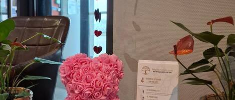 A reception desk with a pink flower arrangement, a printed document, and two potted plants.