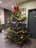 A Christmas tree with ornaments and lights, a red bow, and a clock on the wall.