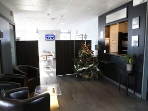 Een receptie met een kerstboom, lederen fauteuils, een receptiebalie en een televisiescherm.