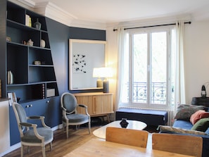 Ein Wohnzimmer mit einer Couch, Sesseln, einem Tisch, einem Bücherregal und einem großen Fenster mit Aussicht.