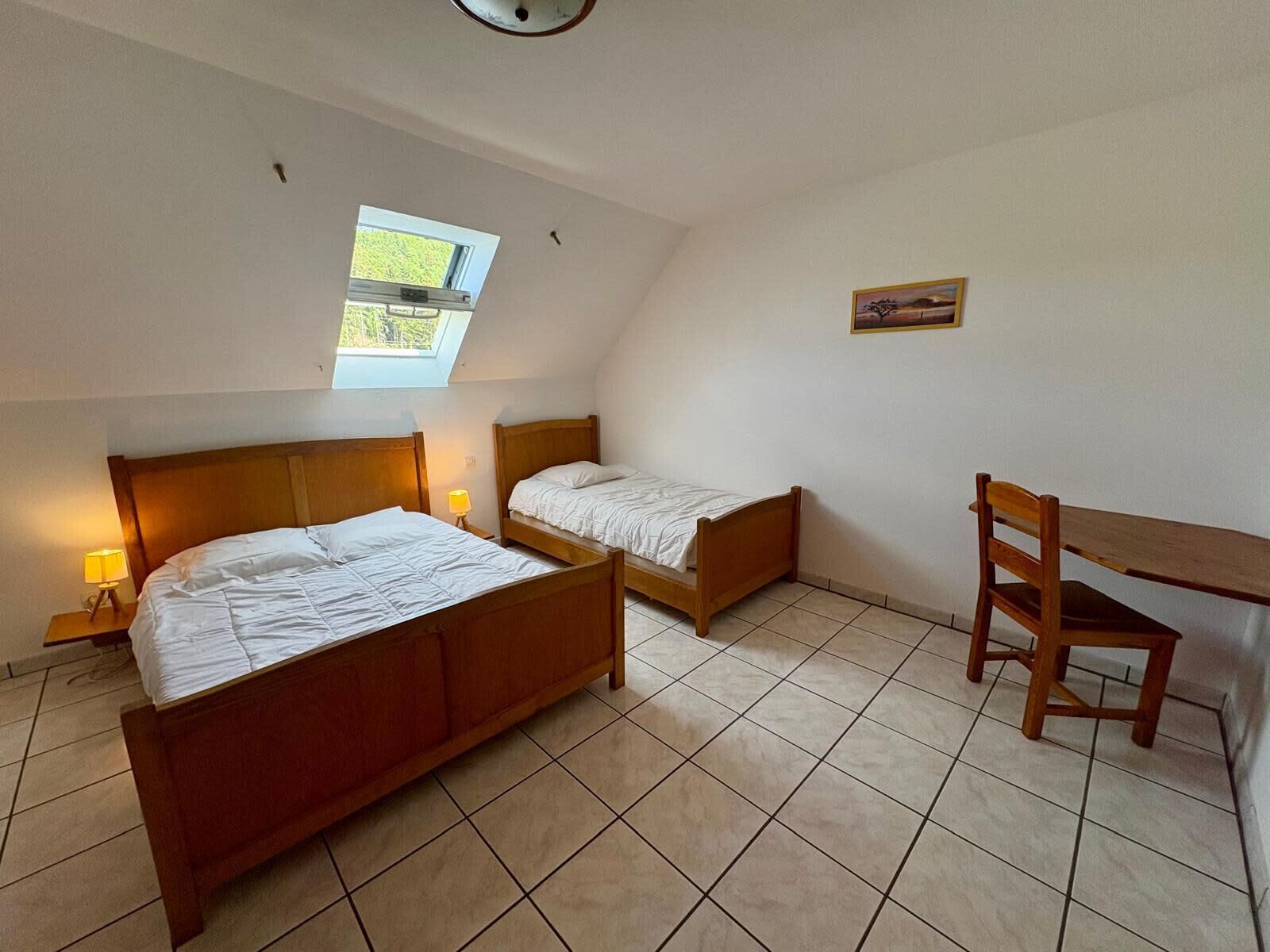 A bedroom with two wooden beds, a desk, and a chair.