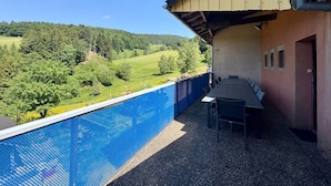A poolside area with a view of a green landscape, a table with chairs, and a building with a sloped roof. - Large house with garden and terrace in Lapoutroie (Lapoutroie)