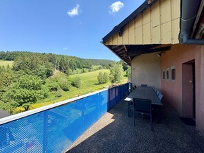 Ein Poolbereich mit Blick auf eine grüne Landschaft, ein Tisch mit Stühlen und ein Gebäude mit schräg stehendem Dach.