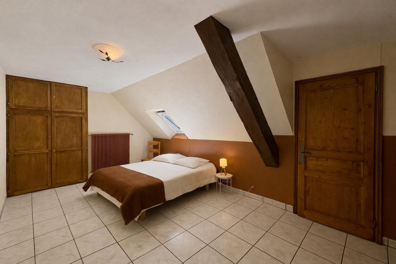 Un dormitorio con techo inclinado, cama, mesita de noche, radiador y puertas de madera.