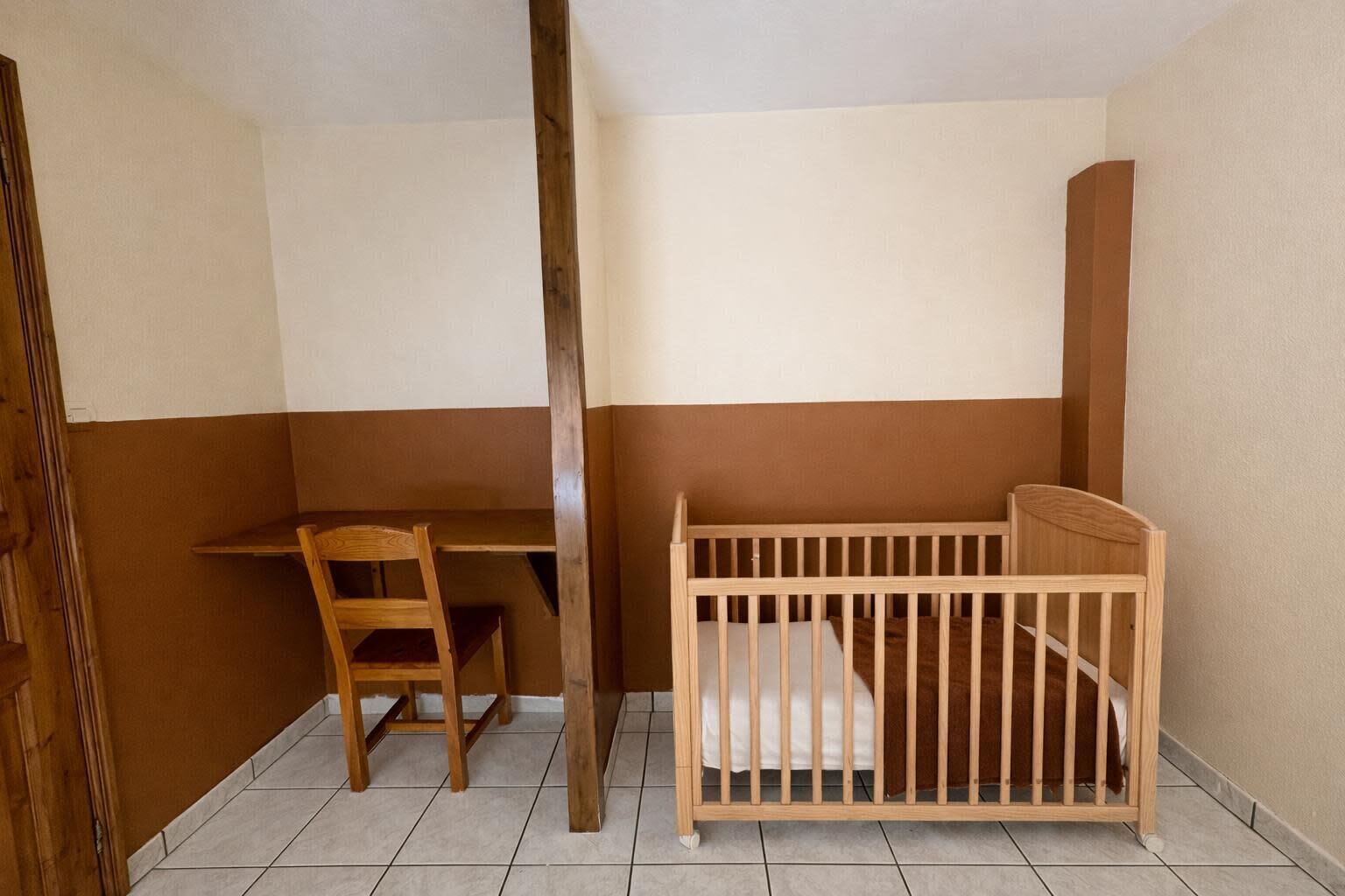 A room with a wooden desk, a chair, and a wooden crib.