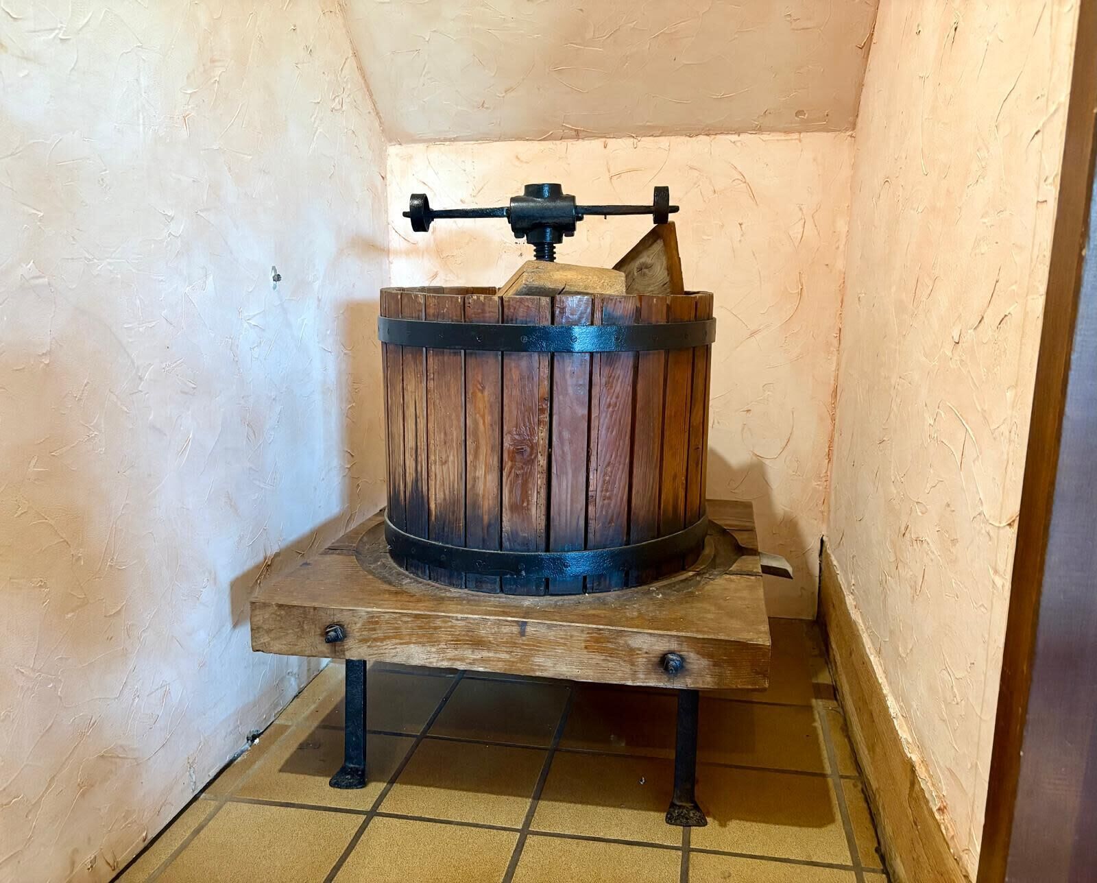 A wooden barrel with a metal mechanism on a wooden base in a corner.