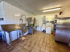 Ammattikäyttöön tarkoitettu keittiö, jossa on ruostumattomasta teräksestä valmistetut laitteet, laatoitettu välitila ja laatoitettu lattia.