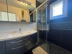 Un baño moderno con cabina de ducha de vidrio, un espejo grande y un ventanal que aporta luz natural.