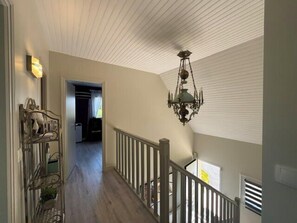 Un pasillo con suelo de madera, un candelabro y una escalera con barandillas blancas.