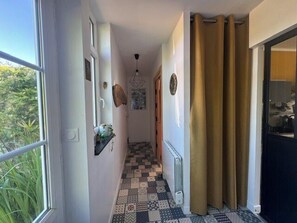 A hallway with patterned flooring, a radiator, a door with curtains, and a window with greenery outside.