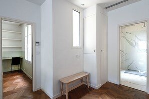 Ein Korridor mit einer Holzbänklä, einer Tür mit Fensterglas und einem kleinen Fenster.
