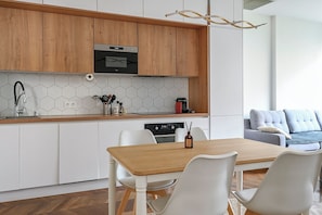 Eine moderne Küche mit Holzschränken, einem eingebauten Ofen, einer weißen Küchenrückwand und einem Essbereich mit Holztisch und weißen Stühlen.