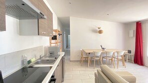 A modern kitchen with a built-in oven, a dining area with a wooden table and chairs, and a red curtain on the right. - Spacious Family Holiday Home with Pool near Uzès – Sleeps 4 (Saint-Siffret)