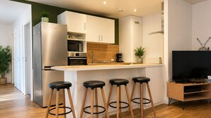 Une cuisine moderne dotée d’un îlot central, de tabourets de bar, d’un four à micro-ondes, d’un four traditionnel et d’un téléviseur posé sur un meuble en bois.