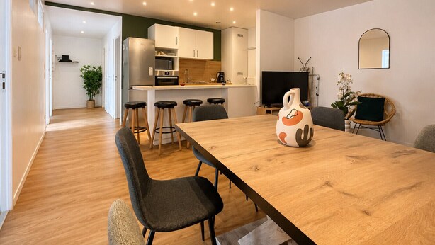 Une cuisine moderne dotée d’un îlot central, un coin repas avec une table en bois et un espace de vie comprenant un téléviseur et des sièges.