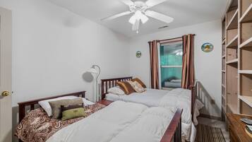 A bedroom with two beds, a ceiling fan, a window with curtains, and a wooden bookshelf.